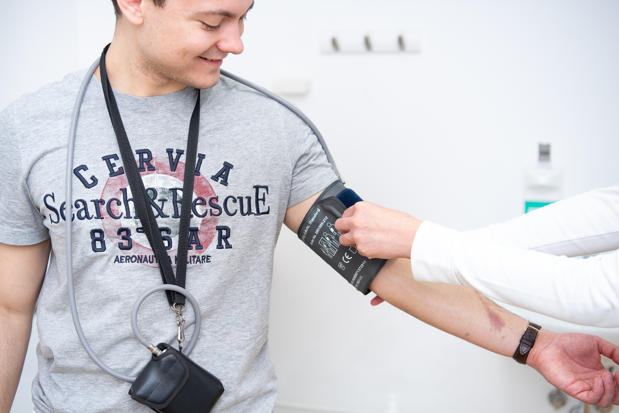 Ein Patient sieht zu, wie die Ärztin mit beiden Händen das 24-Stunden-Blutdruckmessgerät am Oberarm befestigt.