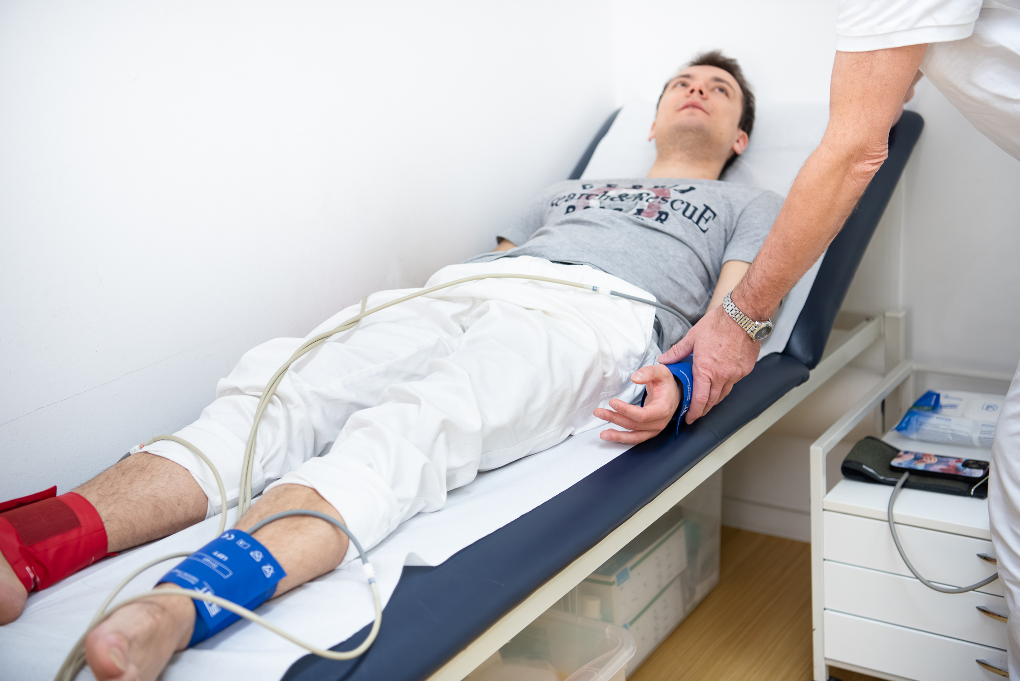 Die Hände des Arztes beim Befestigen des Geräts für die Oszillographie der Arterien. Der Patient blickt zum Arzt.
