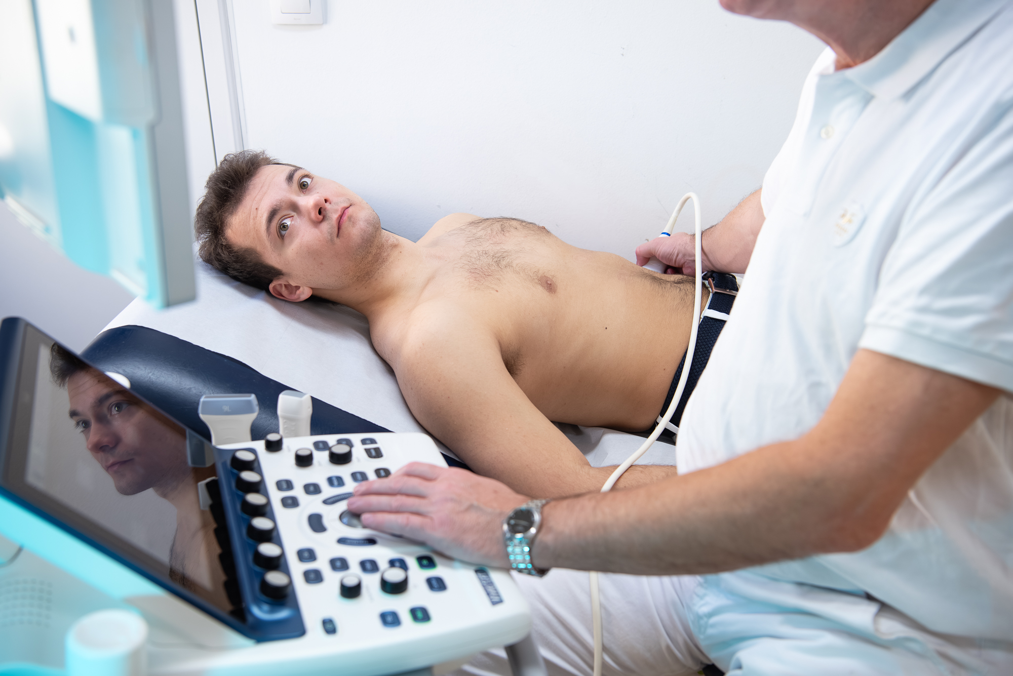 Der Arzt bedient das Untersuchtungsgerat und beobachtet den Bildschirm während der Patient zum Arzt blickt.