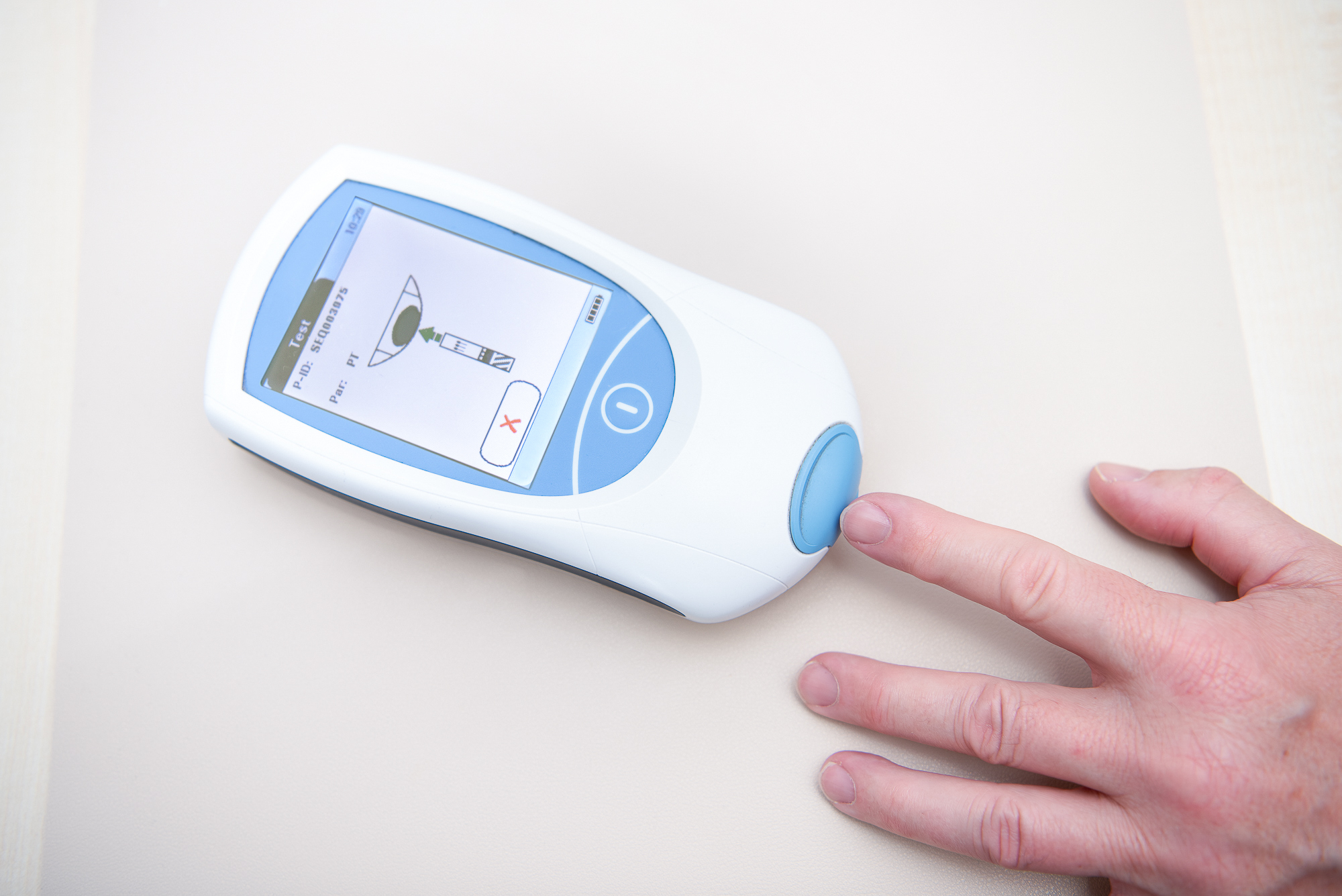 Kleines Gerät zur Bestimmung des INR-Werts und eine Hand, die das Gerät berührt.